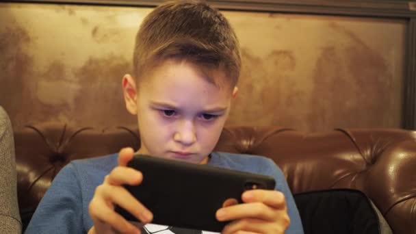 Een tiener speelt aan de telefoon. de reflectie van het scherm zit op het gezicht. zittend op een zachte leren bank, in een kamer met warm licht — Stockvideo