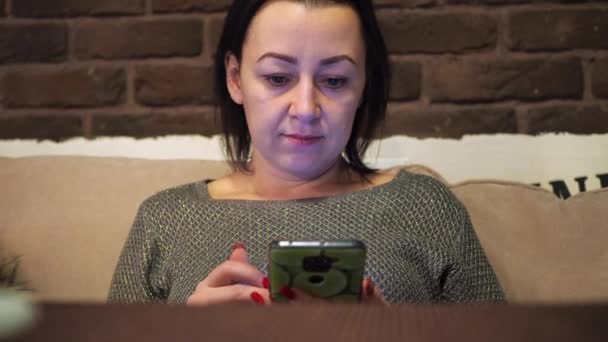 Una ragazza in un caffè a un tavolo legge messaggi in uno smartphone. lavorare in remoto in vacanza — Video Stock