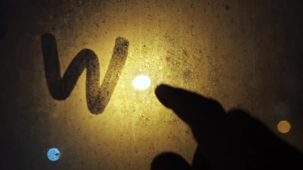 Una mano de hombre escribe una inscripción en el vidrio empañado-invierno. nieve fuera de la ventana a la luz de una linterna ardiente. tex está en la ventana — Vídeo de stock