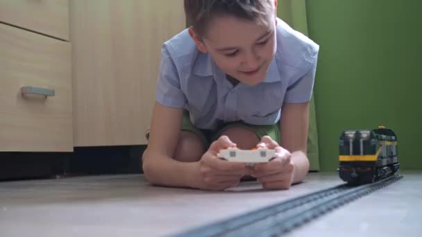 一个11岁的男孩正在房间地板上的控制台上玩火车。侧面看 — 图库视频影像
