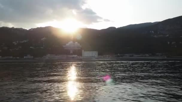 Coucher de soleil. vue de la mer au littoral. région montagneuse avec des hôtels près de l'eau. le soleil jaillit de derrière les montagnes. silence sur la mer — Video