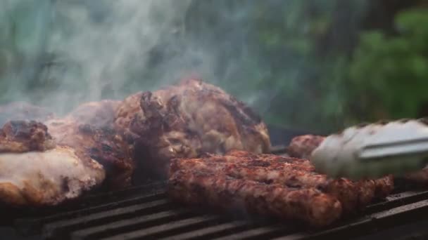 Avec des pinces, il enlève les saucisses frites sur le gril sur les charbons. il y a de la fumée des charbons — Video