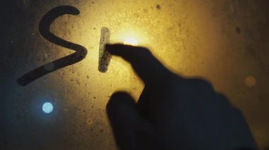 Bir adam sisli cama bir yazı yazar: Kar. Yanan bir fenerin ışığında pencerenin dışında kar. Pencerenin üzerinde.