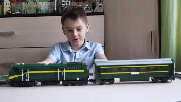 Un garçon assis à une table montre une locomotive avec des wagons. Parlez-moi du constructeur. avis d'un jeune blogueur sur jouets — Video