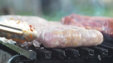 Sosisler ızgarada pişen kömürde kızartılır. Maşayla ters çevir. Lezzetli yemek. Daha fazla çiğ sosis.