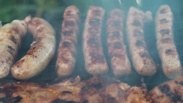 Kupaty gegrild op kolen koken op de grill. Draai het om met een tang. ongezond en vettig voedsel. rook van de grill. zijaanzicht — Stockvideo