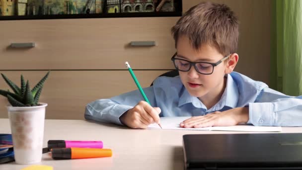 Ein Teenager im blauen Hemd schreibt Hausaufgaben in ein Notizbuch. sitzt an einem Schreibtisch. Hausunterricht — Stockvideo