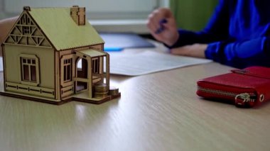Kadın kontratı imzalıyor. Emlakçı kağıtları verir. Sonra anahtarları verir. Masanın üzerinde ahşap bir ev var, evin anahtarları.