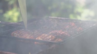 Bir adam kömürün üzerindeki etle ızgarayı çevirir ve bıçakla tavuk parçalarının hazır olduğuna bakar.