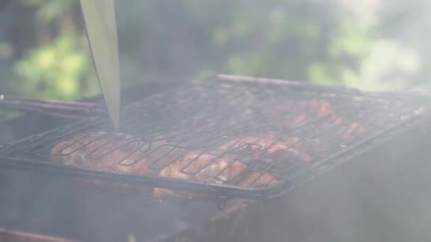 Ręka człowieka obraca grill z mięsem nad węglami i patrzy na gotowość kawałków kurczaka z nożem — Wideo stockowe