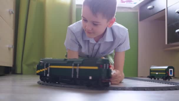 一个11岁的男孩正在房间地板上的控制台上玩火车。侧面看 — 图库视频影像