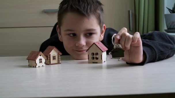Barnet håller ut en nyckelring med nycklarna till den nya lägenheten. det finns leksakshus på bordet.köp av fastigheter. vackra nycklar till den nya byggnaden — Stockvideo