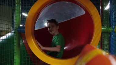 Çocuk bir çocuk kaydırağının içine yuvarlanıyor. Elini sallıyor. Çocuklar için eğlence merkezi