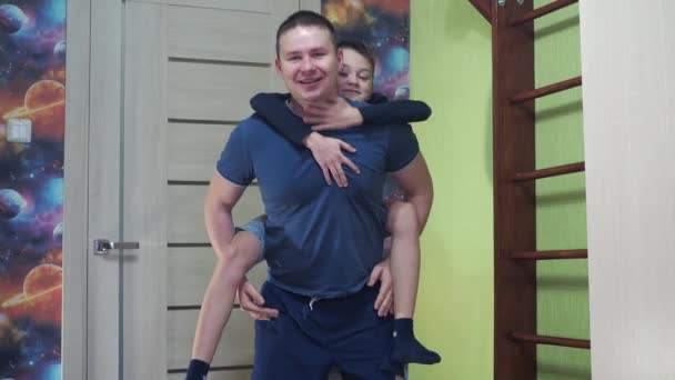 Młody mężczyzna przykuca ze swoim synem na plecach. zajęcia fitness. sport w domu — Wideo stockowe