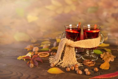 Autumn, autumn leaves, two glasses of hot wine wrapped in one scarf on a wooden table. Seasonal drink, relaxing Sunday and the concept of warmth, care and love. Autumn background, copy space.