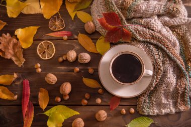 Autumn, fall leaves, hot cup of coffee and warm scarf on wooden table background, top view, copy space. Seasonal, morning coffee, sunday rest and still life concept.