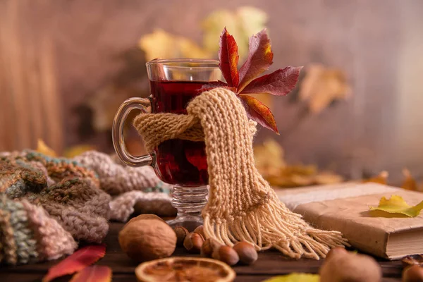 A glass of hot wine wrapped in a warm scarf on a wooden table background, copy space. Autumn, autumn leaves. Seasonal drink, relaxing sunday and warmth and comfort concept.
