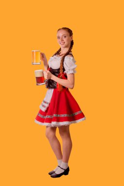 sexy oktoberfest waitress dressed in traditional dirndl (dirndl) dress serving big mug of beer on yellow background
