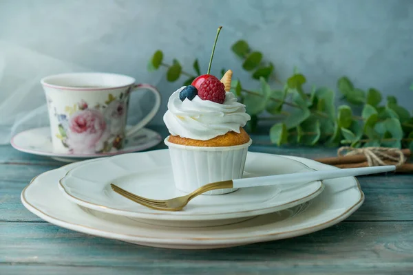 Vanilla cupcake with fruits, a cup of hot tea, on a wooden table, side view, copy space. Seasonal, morning Sunday breakfast and rest.