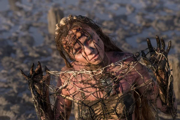 The concept of plastic pollution of the marine environment and conservation of nature - an injured mermaid tangled in a net, stained with fuel oil, suffering from dirt and debris.