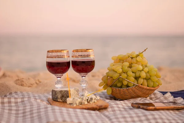 Two glasses of wine, cheese and fruits, close-up on the background of the sea. Joint trip to the sea. Romantic date. Copy space.