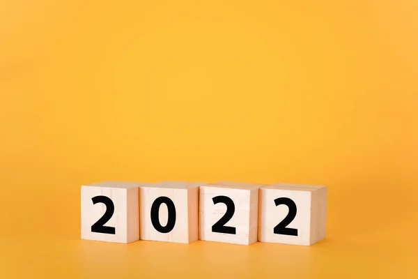 Sarı arka planda ahşap küpler ve 2022. Yeni yıl ve tatil kavramı..