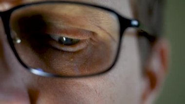 Gece geç saatlerde kameraya bakan gözlüklü bir erkek. Karanlıkta dizüstü bilgisayar kullanan bir programcı, programcı ya da geliştirici. Yansımalı gözlüklerin yakın çekimi.