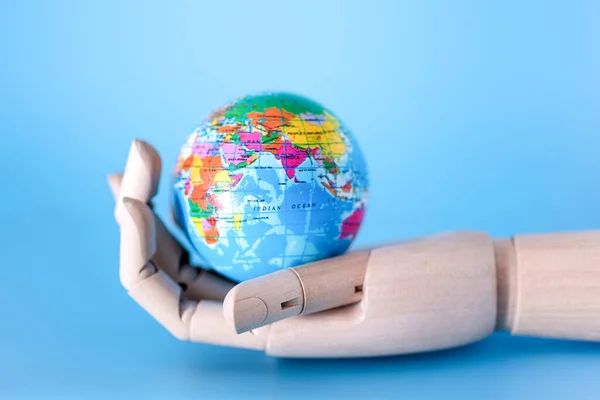 Close-up of a wooden hand holding a mini peace ball against a blue background. The concept of saving the Earth.