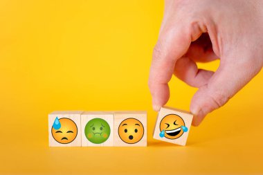 Sarı arka planda Emoji simgeleri var. El, gülen emojili bir küp alıyor. Dünya duygu simgelerinin günü konsepti.
