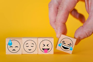 Sarı arka planda Emoji simgeleri var. El, gülen emojili bir küp alıyor. Dünya duygu simgelerinin günü konsepti.