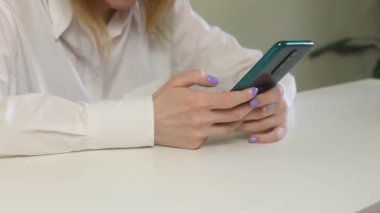 Bir kız telefonuyla masasında oturuyor ve çalışıyor. Telefonda çalışma konsepti..