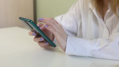 Bir kız telefonuyla masasında oturuyor ve çalışıyor. Telefonda çalışma konsepti..