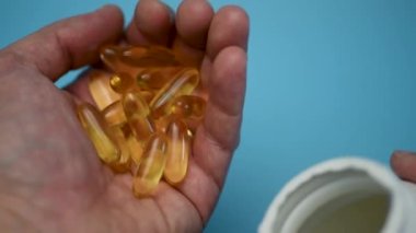 Bir adam eline bir kapsül balık yağı döküyor. Omega 3 'e yakın çekim. Omega 3 Altın balık yağı kapsülleri.