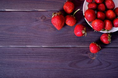 Koyu ahşap arka planda beyaz tabakta taze çilekler. Taze ve sağlıklı yiyecek kavramı.