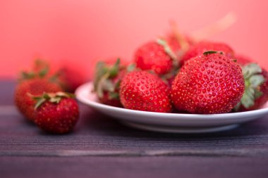 Koyu ahşap arka planda beyaz tabakta taze çilekler. Taze ve sağlıklı yiyecek kavramı. Boşluğu kopyala.