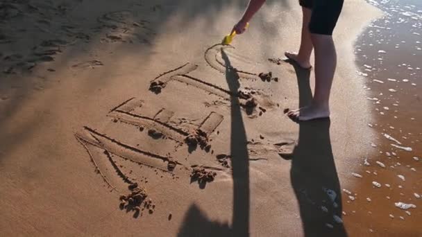 Ein Kind schreibt das Wort Sommer in russischen Buchstaben in den Sand am Strand — Stockvideo