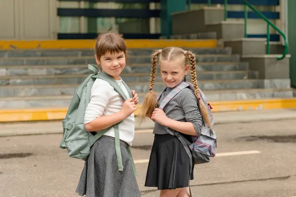 Две милые счастливые девочки школьницы с рюкзаками играют рядом со школой — стоковое фото