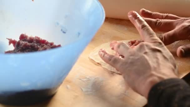 Un uomo in cucina a casa prepara dolci sul tavolo, stende l'impasto, mette la carne macinata a casa concetto di pasto — Video Stock