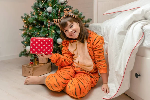 Dziecko uśmiechnięta dziewczyna 9 lat z ciemnymi włosami w stroju tygrysa jako symbol 2022 trzymając prezent w rękach zbliżenie patrzy w aparat Obraz Stockowy