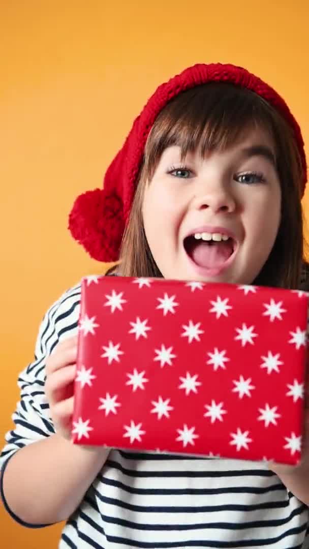 Bonito menina no santa chapéu emocionalmente se alegra no presente no isolado amarelo fundo de perto — Vídeo de Stock