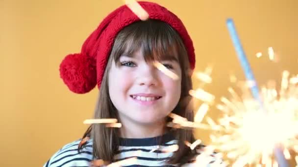 Χαρούμενο κορίτσι παιδί σε καπέλο santa με sparklers σε απομονωμένο κίτρινο φόντο — Αρχείο Βίντεο