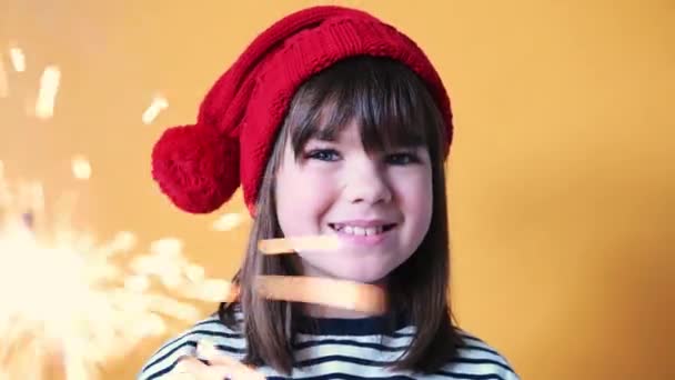เด็กสาวมีความสุขในหมวกซานต้าที่มีแสงสว่างบนพื้นหลังสีเหลืองที่โดดเดี่ยว แนวคิดคริสต์มาส — วีดีโอสต็อก