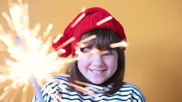 노란 배경의 크리스마스 컨셉트에 스파클러 와 산타 모자를 쓴 행복 한 여자 아이 — 비디오