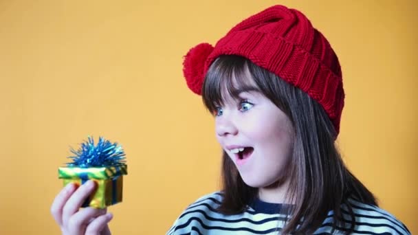 Χαριτωμένο κορίτσι στο καπέλο Σάντα συγκινείται συναισθηματικά στο δώρο σε απομονωμένο κίτρινο φόντο από κοντά — Αρχείο Βίντεο