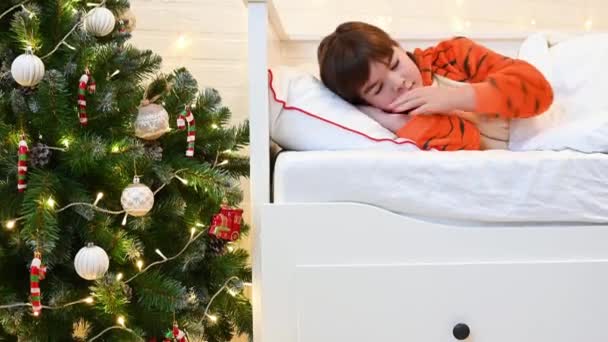 Девушка в костюме тигра спит рядом с рождественской ёлкой в ожидании Рождества и подарков — стоковое видео