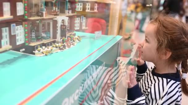 27,11,2021 Ρωσία κορίτσι της Μόσχας ένα παιδί στέκεται σε μια βιτρίνα με έναν κατασκευαστή Lego σε ένα εμπορικό κέντρο κοιτάζει από κοντά — Αρχείο Βίντεο