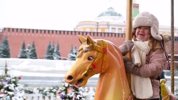 Criança menina monta um cavalo em um alegre-go-round na praça vermelha em moscow no inverno — Vídeo de Stock