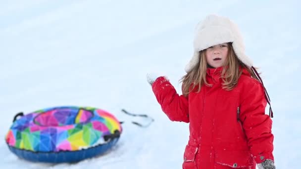 Malá legrační dívka v červené bundě s nafukovací trubice projíždí po tobogánu ve sněhu v zimě — Stock video