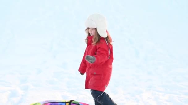 冬天，身穿红色夹克、头戴充气管子的小女孩在雪地里滑行 — 图库视频影像