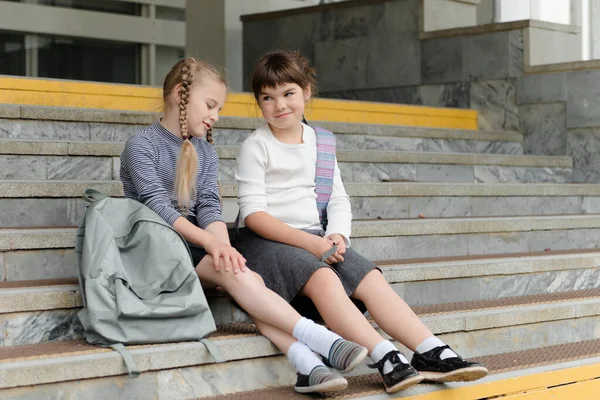 Две милые счастливые девочки школьницы с рюкзаками играют рядом со школой — стоковое фото